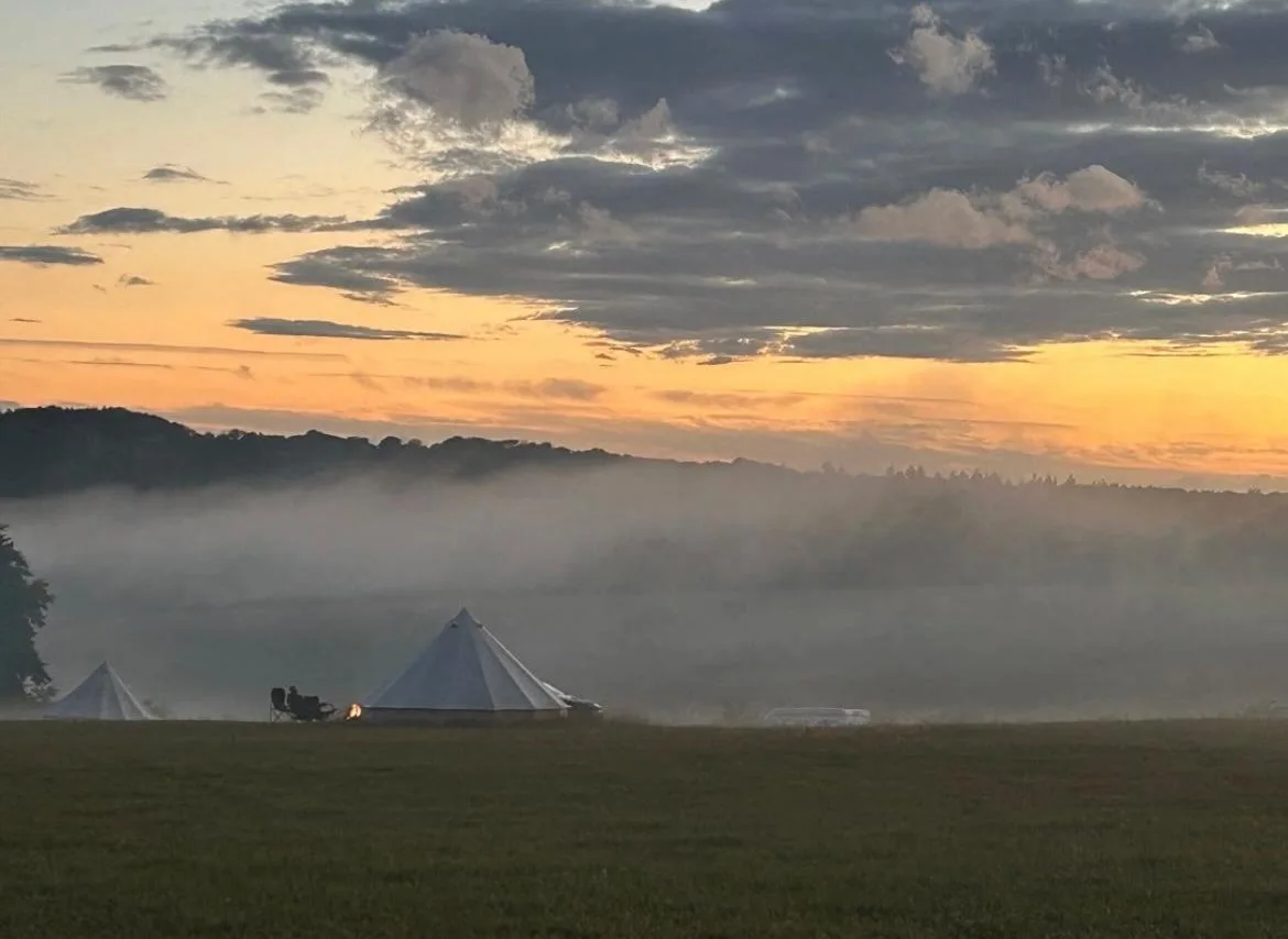 Bell tents on the field at dawn, mist across the valley and a lit campfire